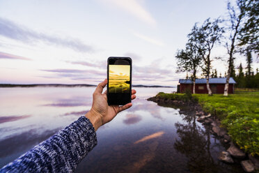 Schweden, Lappland, Person, die ein Smartphone-Foto vom Sonnenuntergang macht - KKAF01977