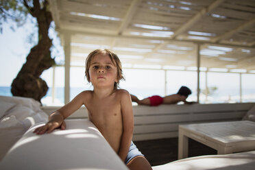 Porträt eines kleinen Jungen, der sich in einer Lounge am Strand ausruht - AZOF00030