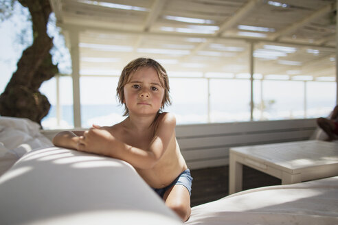 Porträt eines ernsten kleinen Jungen, der sich in einer Lounge am Strand ausruht - AZOF00031