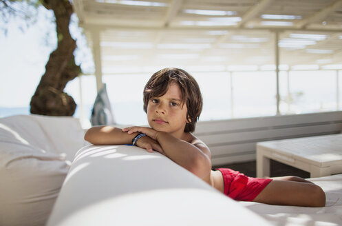 Porträt eines ernsten kleinen Jungen, der sich in einer Lounge am Strand ausruht - AZOF00032