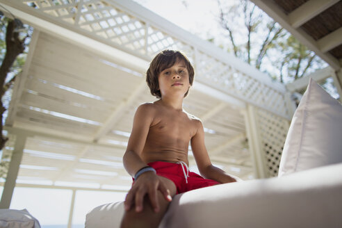 Porträt eines ernsten kleinen Jungen, der sich in einer Lounge am Strand ausruht - AZOF00034