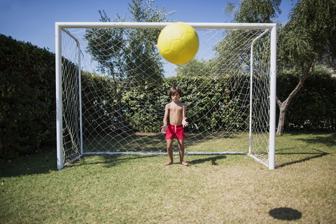 Kleiner Junge steht vor einem Fußballtor und schaut Fußball, lizenzfreies Stockfoto