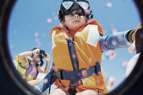 Toddler wearing life jacket and diving goggles with brother in background - AZOF00042