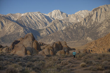 An adult woman trail running in the early morning through a boulder field with a large mountain landscape in the background. - AURF04864