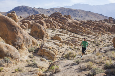 An adult woman trail running in the early morning through a boulder field with a large mountain landscape in the background. - AURF04866