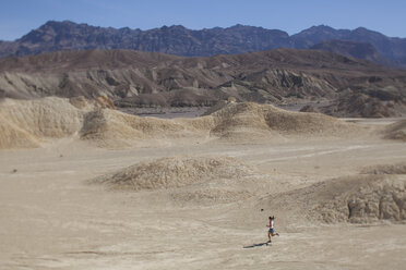 An adult woman running through a harsh dry desert landscape - AURF04867