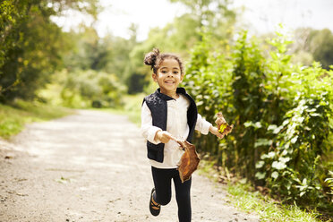 Glückliches kleines Mädchen läuft mit zwei großen Herbstblättern - AURF04946