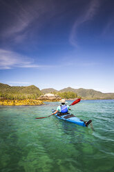 HAIDA GWAII, BRITISH COLUMBIA, CANADA. A woman kayaks through a remote flatwater landscape with mountains in the background. - AURF04962