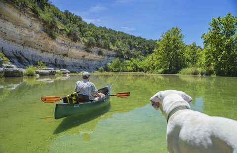 Hund beobachtet Mann im Kanu auf dem Fluss, lizenzfreies Stockfoto