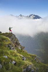 Wanderung auf steilem Grat, mit Wanderstock auf Bergkette im Hintergrund zeigend - AURF05172
