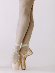 Low section of ballet dancer standing en pointe with slightly crossed legs - AURF05245