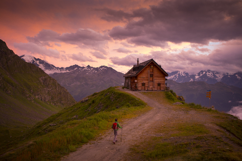 Mann wandert zu einer Berghütte bei Sonnenuntergang, lizenzfreies Stockfoto