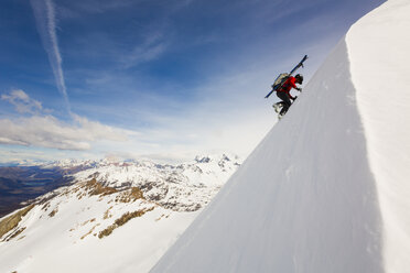 Mann mit Skiern auf dem Rücken besteigt verschneiten Berg - AURF05256