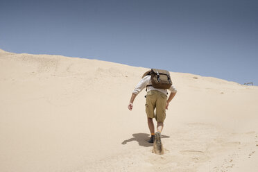 Man with backpack climbing sand dune - AURF05315