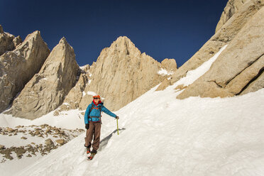 MT. WHITNEY, MOUNTAINEER'S ROUTE, LONE PINE, CA, USA. A 30 year-old woman in mountaineering clothes smiles as she descends a steep snow field with jagged granite peaks rising behind her. - AURF05339