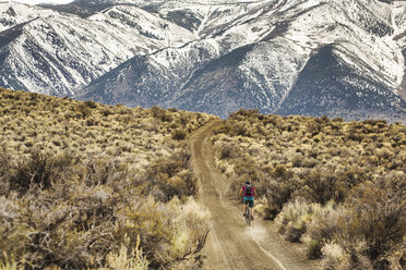 MONO LAKE, CA, USA. A young woman rides a mountain bike down a dirt road with snow-covered mountains in the distance. - AURF05341
