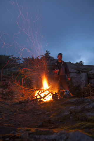 Porträt eines Bergsteigers, der sich neben einem alpinen Lagerfeuer warm hält, lizenzfreies Stockfoto