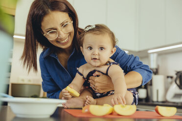 Mutter und kleine Tochter essen Apfelstücke in der Küche - MFF04646