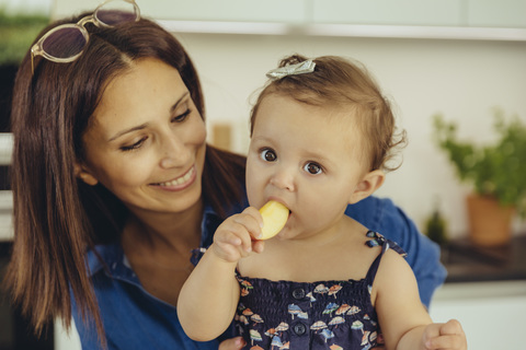 Mother watching baby daughter eating an apple stock photo