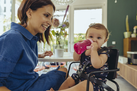 Happy mother watching baby daughter drinking water from bottle stock photo