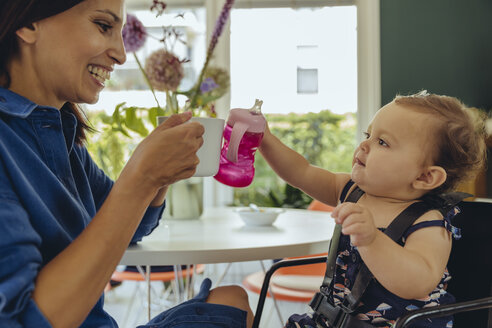 Happy mother and baby daughter clinking coffee cup and baby bottle - MFF04652