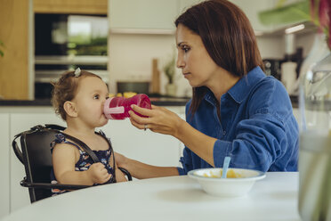 Mutter hilft ihrer kleinen Tochter beim Trinken von Wasser aus der Flasche in der Küche - MFF04654