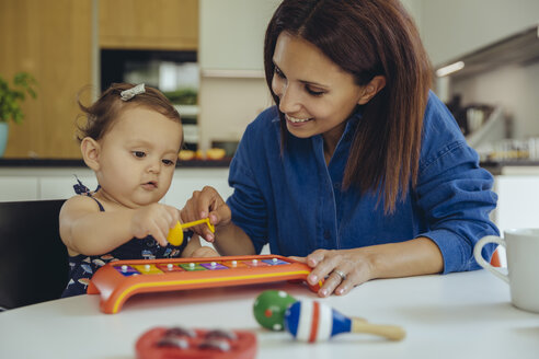 Happy mother and baby daughter playing with a glockenspiel - MFF04658