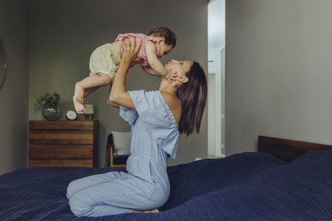 Mutter hebt ihr kleines Mädchen im Bett hoch, lizenzfreies Stockfoto