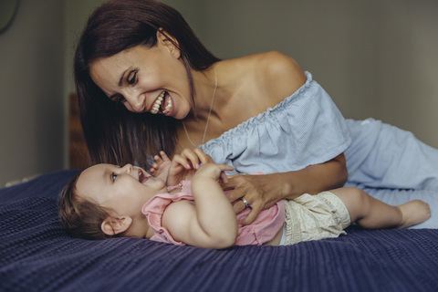 Glückliche Mutter spielt mit ihrem kleinen Mädchen auf dem Bett, lizenzfreies Stockfoto