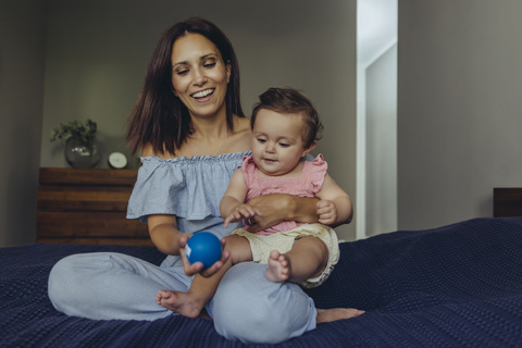 Happy mother playing with her baby girl on bed stock photo