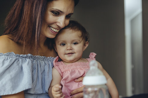 Mutter bietet ihrem kleinen Mädchen Milch in einer Flasche an - MFF04669