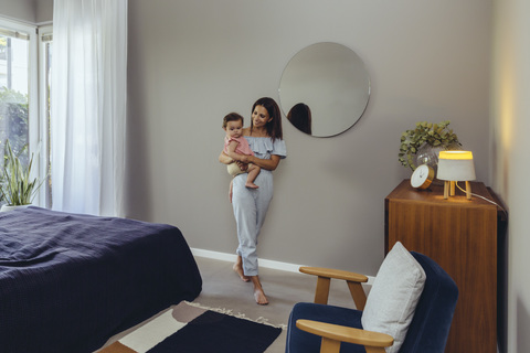 Smiling mother carrying her baby girl at home stock photo