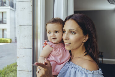 Lächelnde Mutter schaut aus dem Fenster mit ihrer kleinen Tochter zu Hause - MFF04673