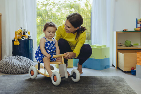 Glückliche Mutter mit kleiner Tochter auf Spielzeugauto im Wohnzimmer - MFF04676