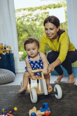 Glückliche Mutter mit ihrer kleinen Tochter, die im Wohnzimmer ein Spielzeugauto fährt, lizenzfreies Stockfoto