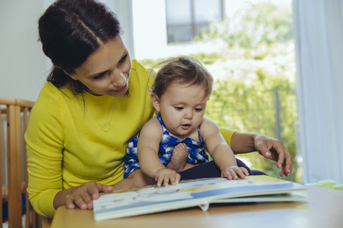 Mutter und kleine Tochter schauen sich ein Kinderbuch an, lizenzfreies Stockfoto