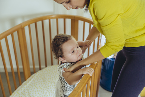 Mother picking up her baby girl from bed stock photo