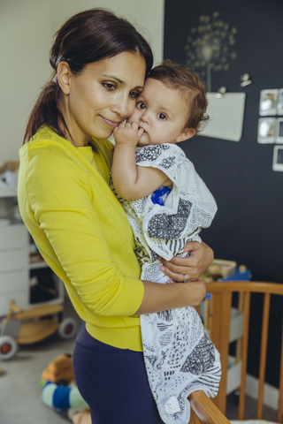 Lächelnde Mutter hält ihr Baby im Schlafsack im Kinderzimmer, lizenzfreies Stockfoto