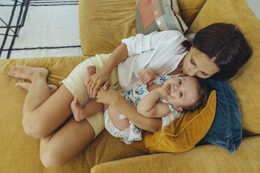Mother cuddling and kissing her baby girl on couch - MFF04694