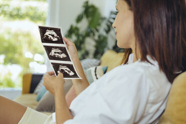 Woman looking at ultrasound pictures of unborn child on couch - MFF04701