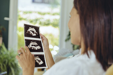 Woman looking at ultrasound pictures of unborn child on couch - MFF04702