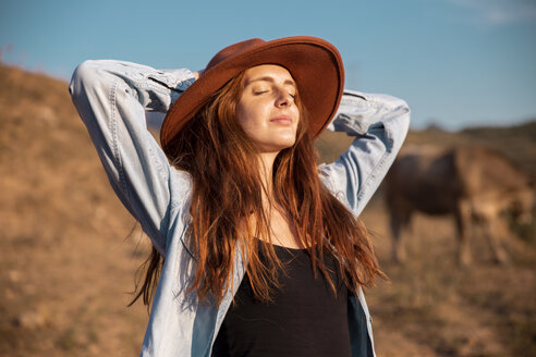 Young woman wearing a hat relaxing and enjoying the rural landscape - AFVF01570