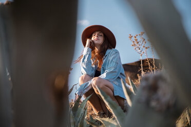 Junge Frau mit Hut sitzt an einer Agave in der Landschaft - AFVF01572