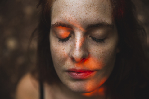 Porträt einer jungen Frau mit Sommersprossen, die ihre Augen schließt, lizenzfreies Stockfoto