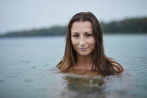 Porträt einer sommersprossigen jungen Frau beim Baden im See an einem regnerischen Tag, lizenzfreies Stockfoto
