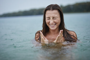 Porträt einer sommersprossigen jungen Frau beim Baden im See an einem regnerischen Tag - PNEF00883