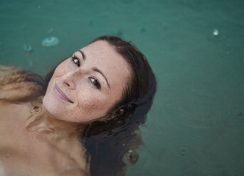 Porträt einer sommersprossigen jungen Frau beim Baden im See an einem regnerischen Tag - PNEF00886