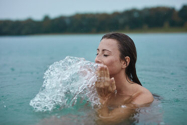 Porträt einer jungen Frau, die in einem See badet und mit Wasser spritzt - PNEF00888