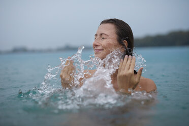 Junge Frau badet in einem See und spritzt mit Wasser - PNEF00892