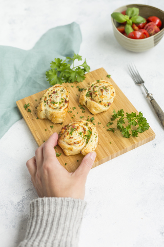 Woman's hand taking sticky bun with feta, cream cheese, bacon and parsley stock photo